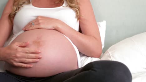 Pregnant-woman-sitting-on-bed-touching-her-belly