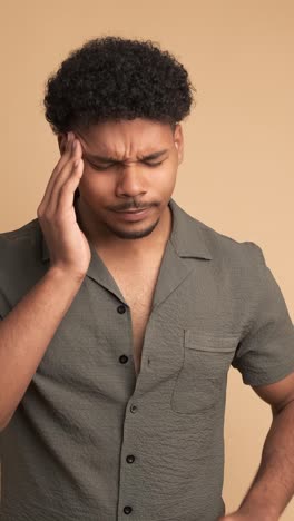 frustrated man suffering from headache in beige studio