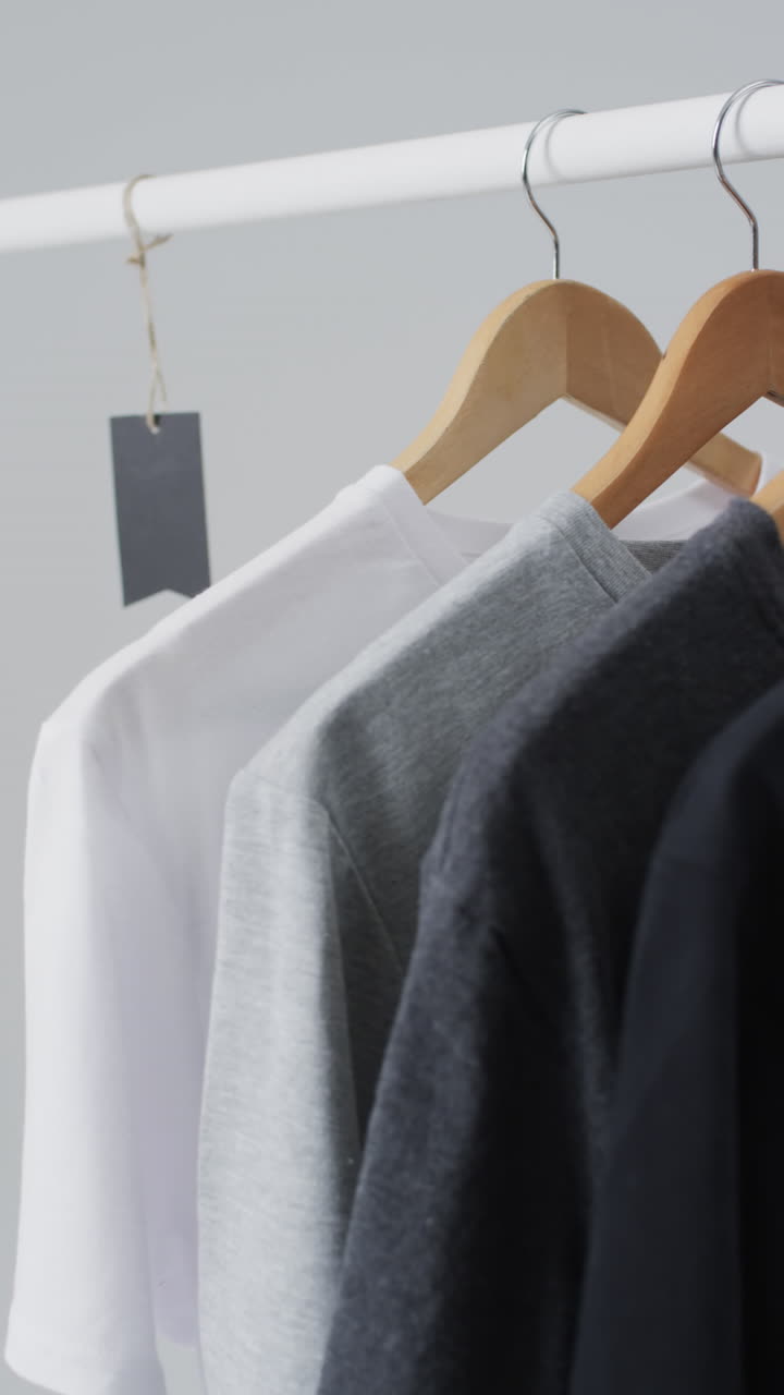 Vertical video of t shirts on hangers and copy space on white background