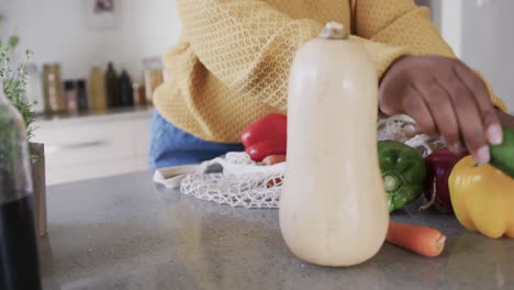 Mid-section-of-african-american-woman-unpacking-groceries-in-kitchen,-in-slow-motion