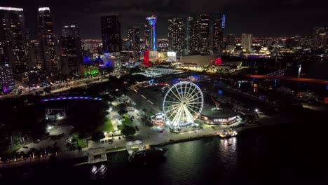 Nächtliche-Stadtlandschaft-Von-Skyviews-Miami-Riesenrad-Am-Bayside-Marketplace-Mit-Spiegelungen-Im-Wasser-Der-Biscayne-Bay-Und-Hohen-Beleuchteten-Wolkenkratzern-Von-Brickell-Bei-Nacht