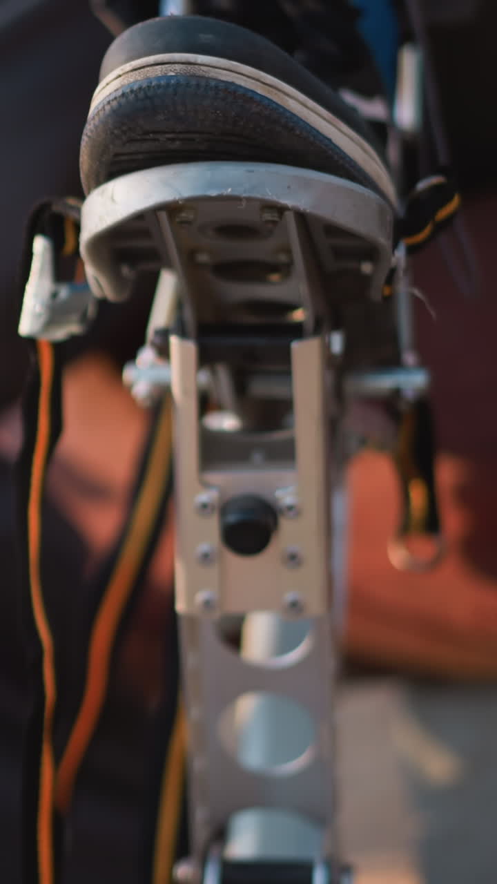 primer plano de los pies del tipo en zapatillas de deporte negras y azules, posicionados en equipos de tiro con arco al aire libre. lleva pantalones oscuros, levantando el equipo ligeramente en luz natural, con vegetación borrosa en el fondo