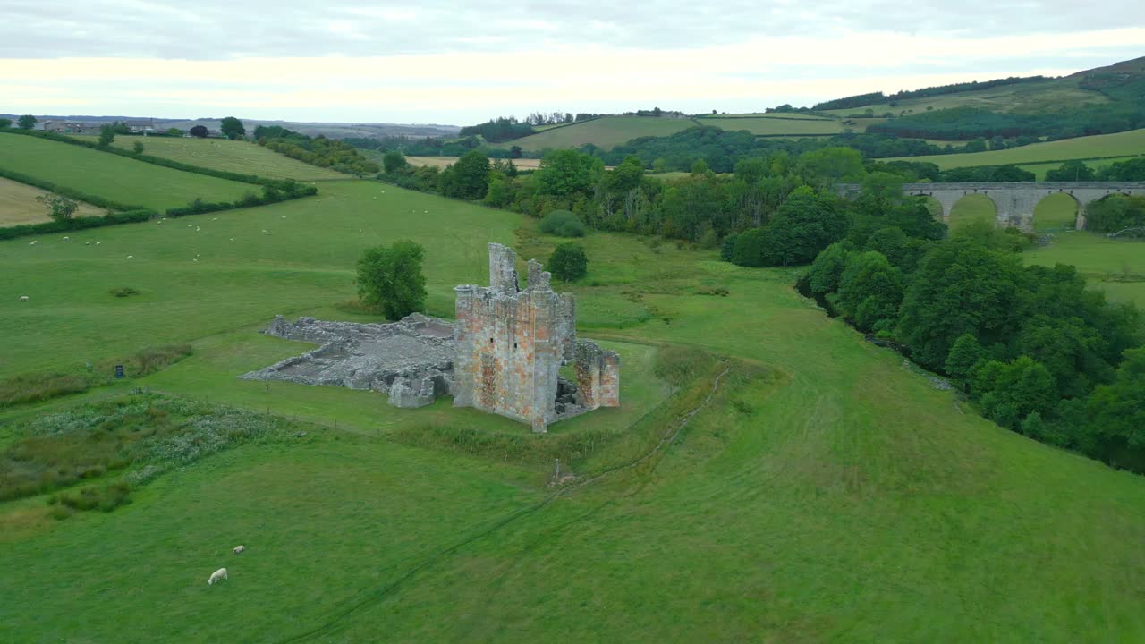 Filmato aereo realizzato con drone che ruota intorno alle rovine di uno storico castello in Inghilterra, con un ponte romano sullo sfondo in una giornata nuvolosa, creando un'atmosfera cupa ed evidenziando l'antica architettura e il patrimonio storico