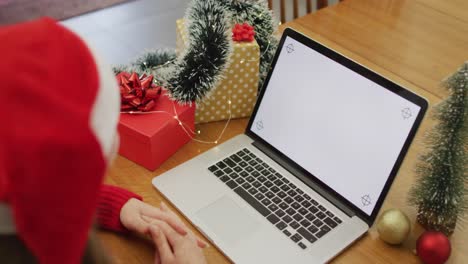 Caucasian-woman-wearing-santa-hat-making-video-call-at-home-on-laptop-with-copy-space-on-screen