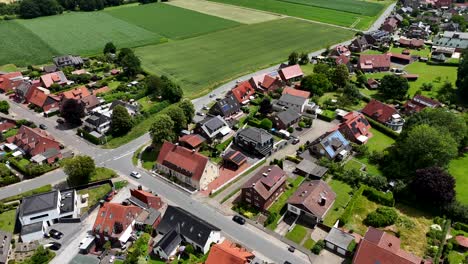aerial view of quiet american suburban neighborhood with single-family homes, sloped roofs, green yards and open fields. peaceful summer atmosphere in a rural-urban edge setting. flyover shot