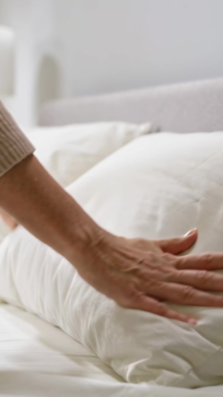 Video verticale: Mani di donna che premono, entrando nell'inquadratura, che battono un cuscino sul letto per renderlo più soffice, indossando un maglione.