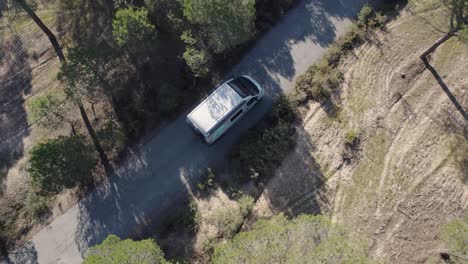 在公路旅行中穿越狭窄的森林农村的露营车后面的空中鸟眼视图