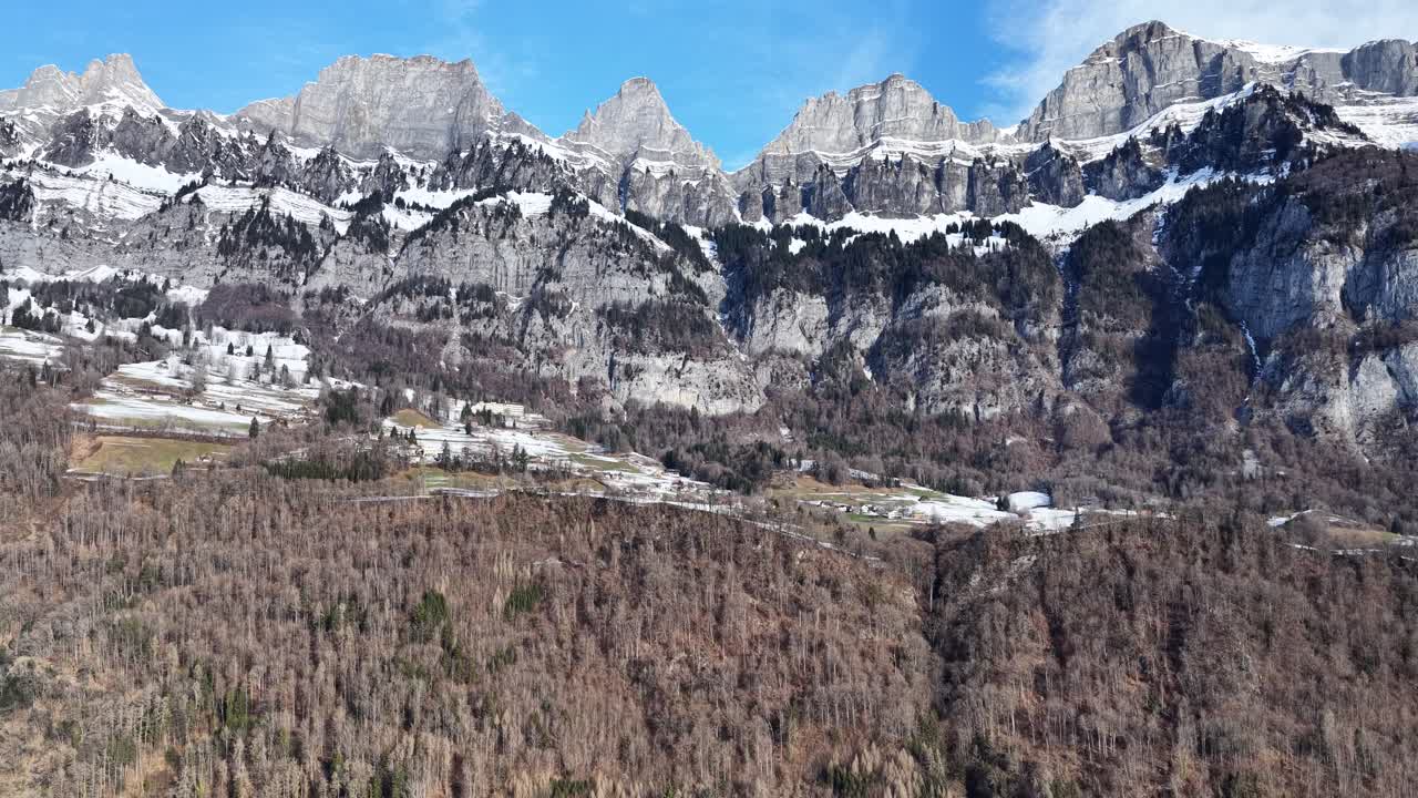 Vista dell'iconica catena montuosa del Churfirsten in Svizzera. Cime calcaree appuntite e innevate si ergono sopra pendii boschivi in un limpido scenario alpino invernale