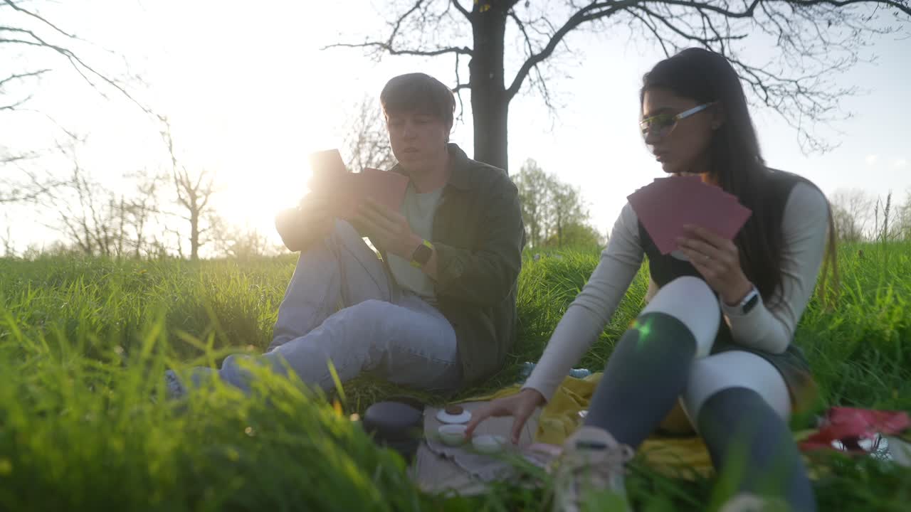 Couple playing cards on a picnic in a park at sunset