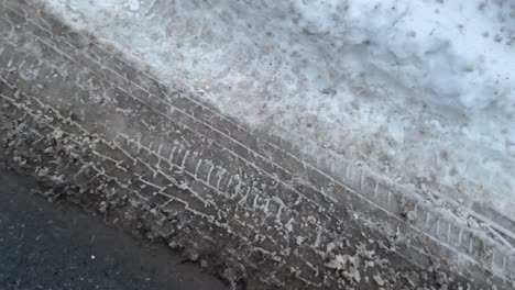 dirty muddy compact snow tire tracks from car tires on road during winter with snow melting into slush with spring coming in canada