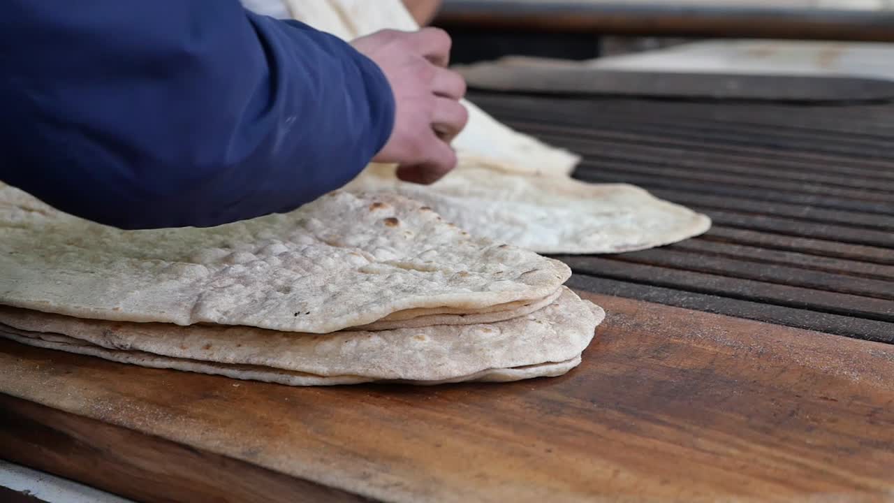 Hands Stacking Freshly Baked Flatbread on a Wooden Board