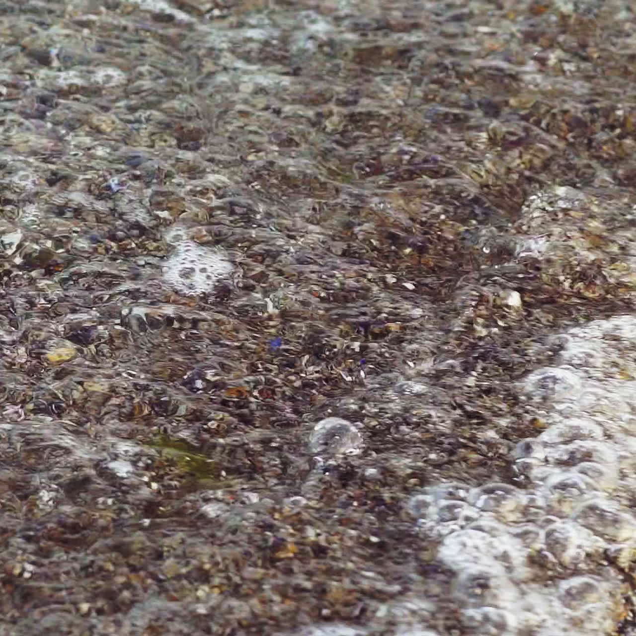 Clean and clear sea water glides over pebbles near the shore in summer. Stone texture. Close-up.