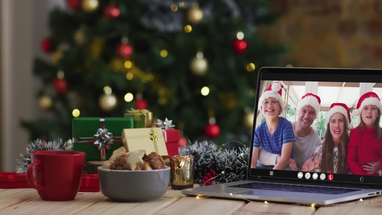 familia feliz usando sombreros snata en videollamada en computadora portátil, con decoraciones de navidad y árbol