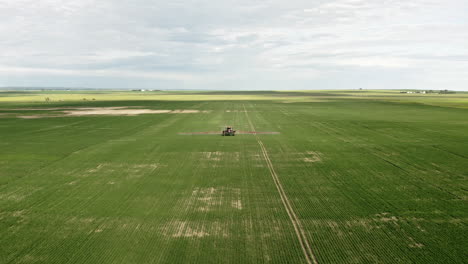 Maquinaria-Agrícola-Rociando-Campos-De-Trigo-Verde-En-Saskatchewan,-Canadá---Drone-Aéreo