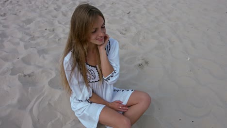 Una-Mujer-Hermosa-Con-Cabello-Largo-Vestida-De-Blanco-Relajándose-En-La-Playa-Y-Disfrutando-Del-Clima