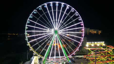 Large Ferris wheel glowing with colorful lights beside Wild Mouse ride at night in Ayia Napa. Ayia Napa, Cyprus