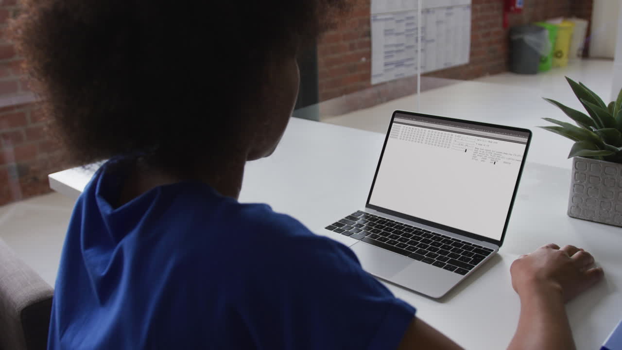 African american woman sitting at desk watching coding data processing on laptop screen