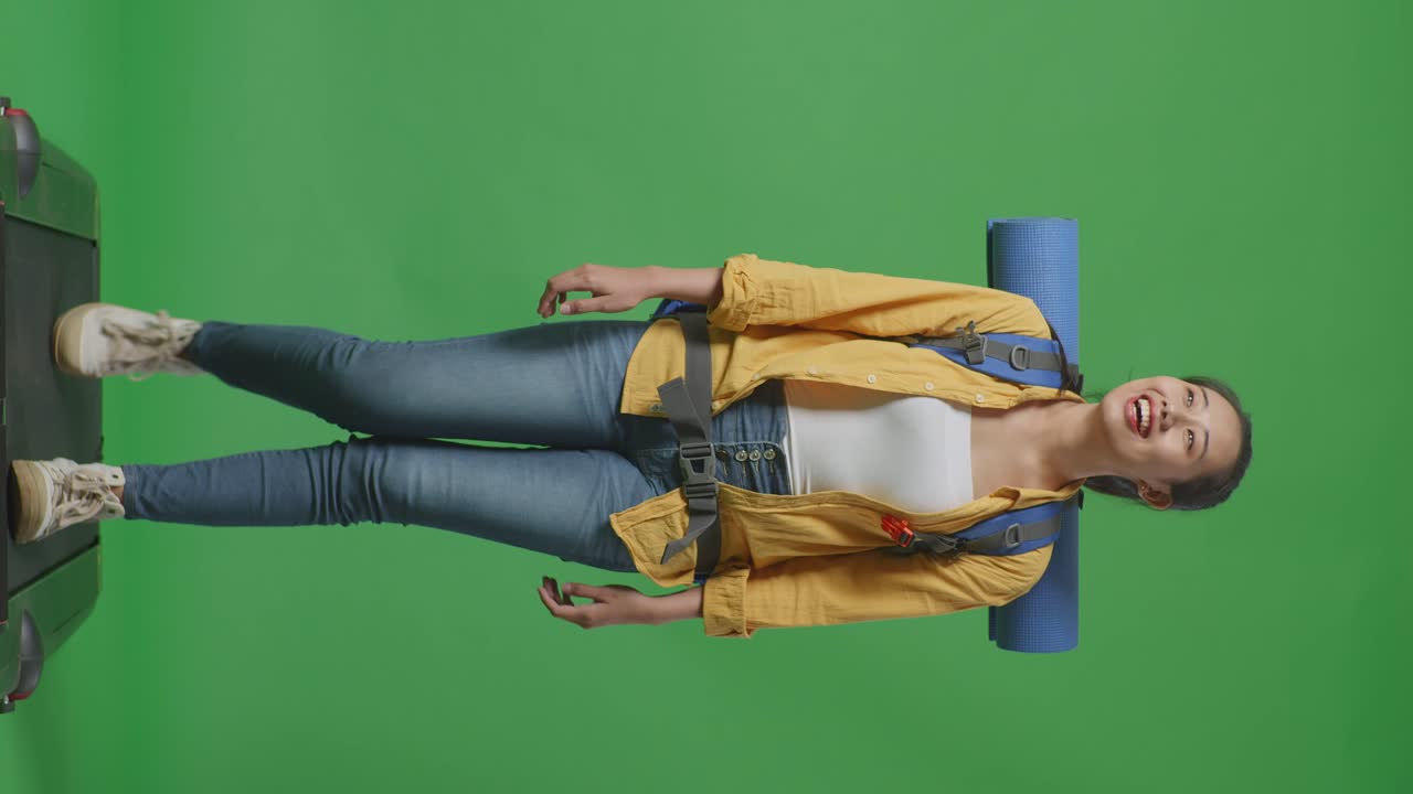 Full Body Of Asian Female Hiker With Mountaineering Backpack Looking Around While Walking On A Treadmill On Green Screen Background In The Studio