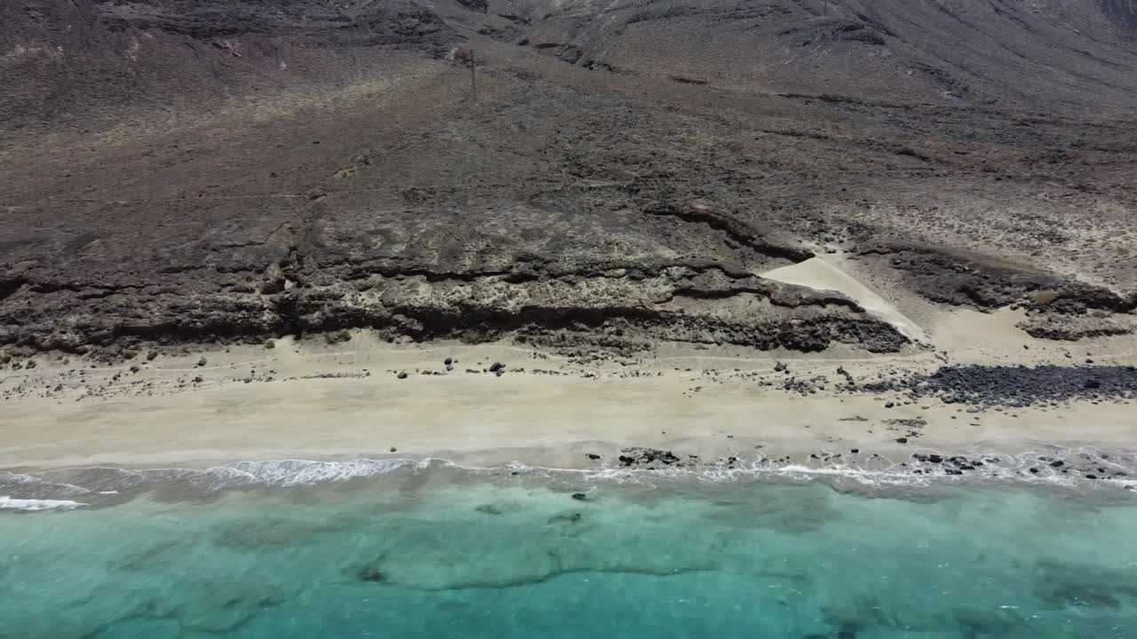 Spiaggia selvaggia e deserta su una costa rocciosa vulcanica, con dolci onde di acqua azzurra