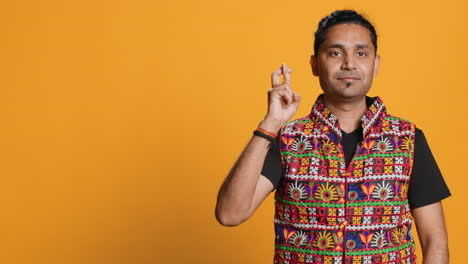 Portrait-of-man-crossing-fingers-and-doing-victory-sign,-studio-background