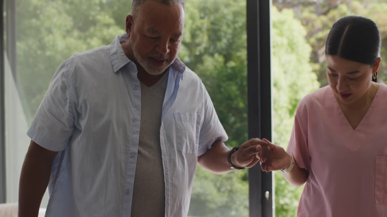 African American man, Asian nurse in pink scrubs steadying hand, guiding through glass door to yard