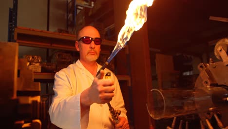 front view of mature male worker lighting glass blowing torch in glass factory 4k