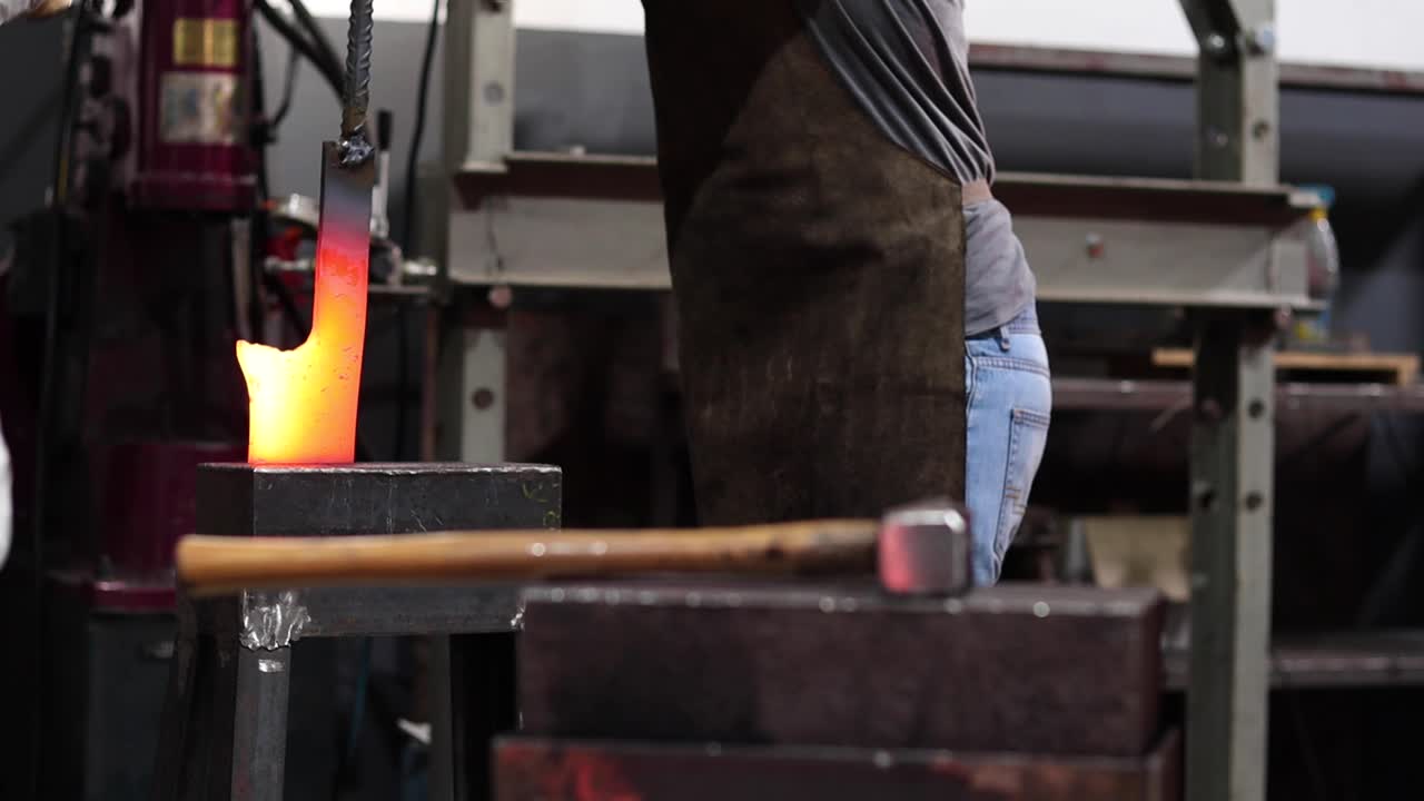 Blacksmiths forging hot metal with hammer in workshop