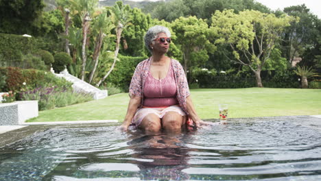 Feliz-Mujer-Afroamericana-Mayor-Sentada-En-El-Jardín-Chapoteando-En-La-Piscina,-Espacio-Para-Copiar,-Cámara-Lenta