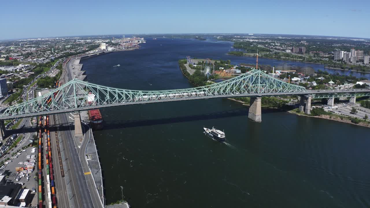 Aerial view of the Jacques Cartier Bridge in Montreal, spanning the St. Lawrence River. Its iconic design and connection between the island and the South Shore, with the city skyline in the backdrop.