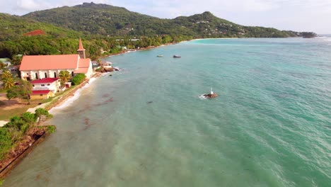 drone de la iglesia de san josé cerca de la orilla de la playa de anse royale, cruz en la roca en el centro del océano, mahe, seychelles 30fps