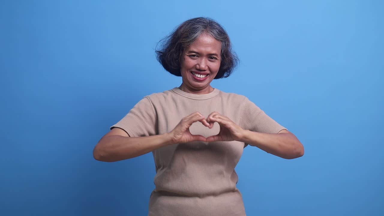 Middle age Asian woman stands cheerfully making heart shape with hands. romantic concept of love beautifully