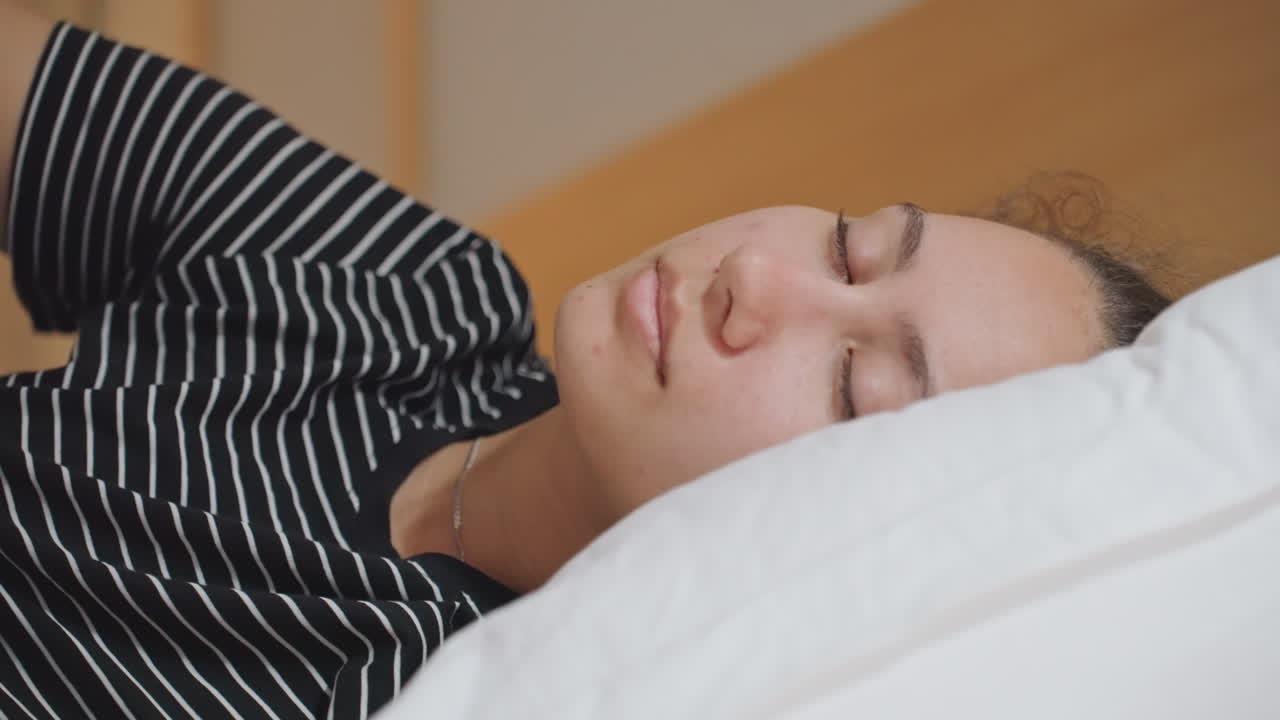 Multietnisk gæst tager en lur i hotelseng, morgenlys filtrerer ind over dynen, afslappet udtryk, armbånd på armen, hyggeligt sengetøj og rolig atmosfære, et stille øjeblik med selvforkælelse under opholdet.