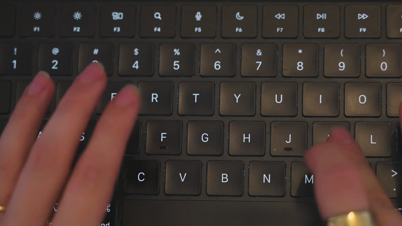 top-down shot of a women's hands wearing jewelry typing on a keyboard