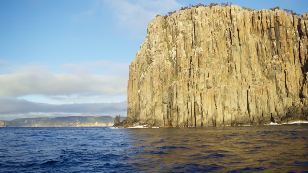 Jagged cliffs rise dramatically from the sea along the Tasmanian coastline, showcasing the region’s wild and remote beauty from the water.