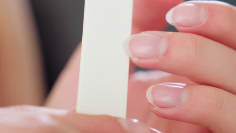 detailed close up of woman filing fingernails with white nail filer, showcasing precision grooming, soft pink nails, clean cuticle edges, and focus on hand care routine in calm indoor atmosphere