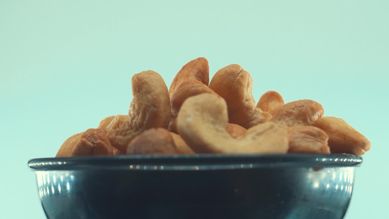 Nærbilde av en ristet saltet cashewnøtt i en svart skinnende bolle på et roterende stativ, sakte film, 4k