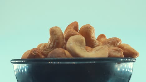 a close up shot of a roasted salty cashew in a black shiny bawl on a rotating stand, slow motion, 4k