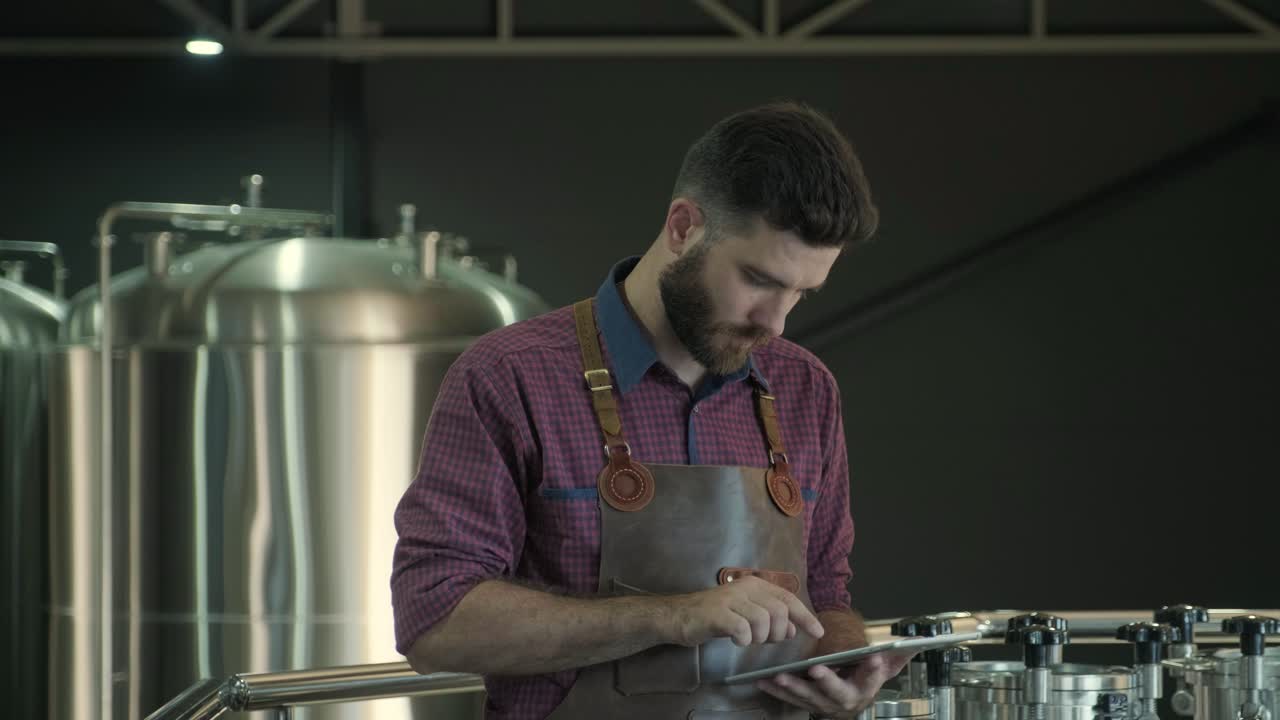 un joven cervecero con un delantal de cuero supervisa el proceso de fermentación de la cerveza en una fábrica de cerveza moderna