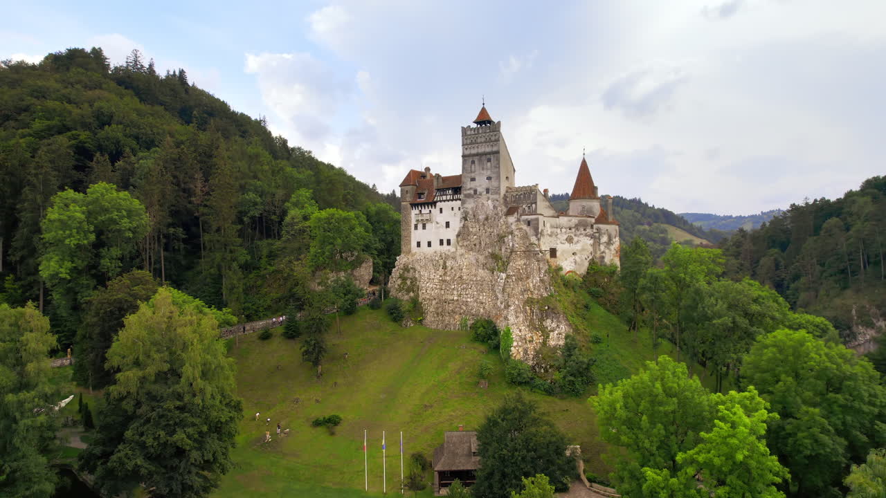 Letecký pohled dronem na hrad Bran v Rumunsku. Středověký hrad v Karpatech, zelené stromy kolem, procházející se turisté