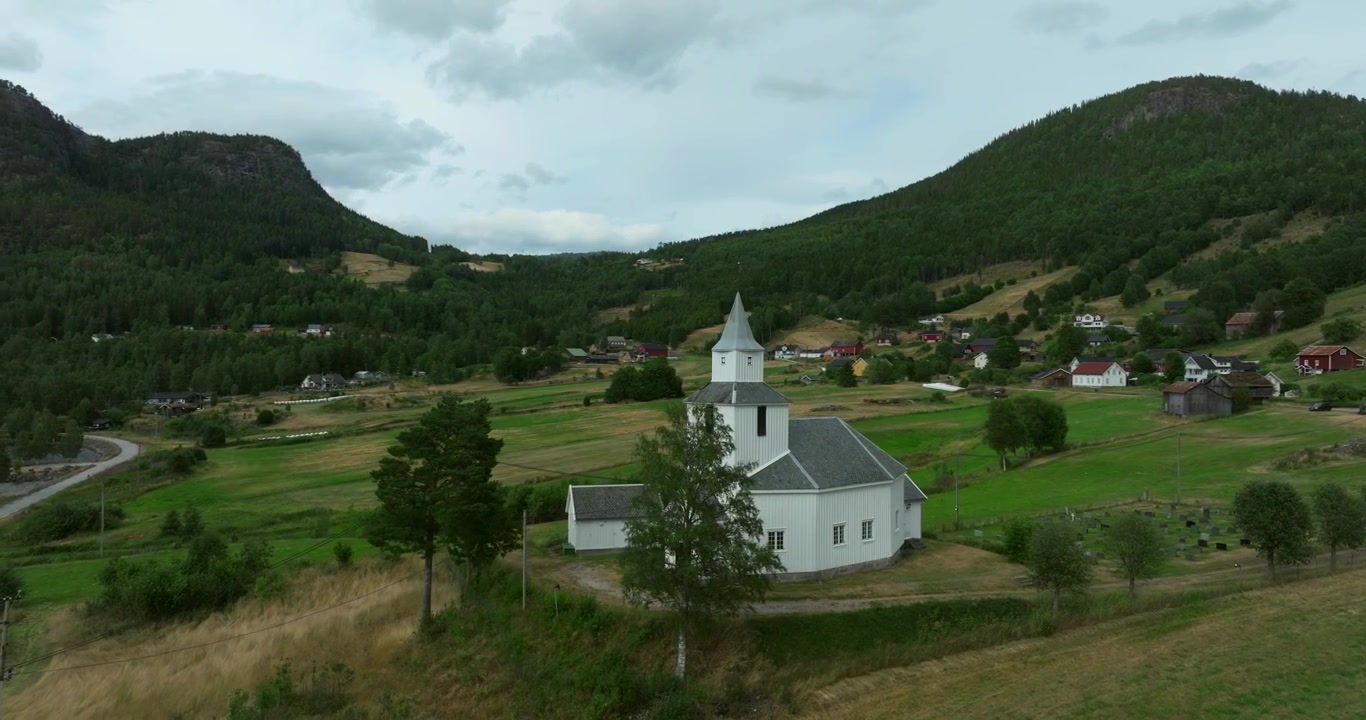 Flygfoto av vit kyrka vid sjö i Bygland, Norge, som visar dagsljus och ett förhöjt perspektiv.