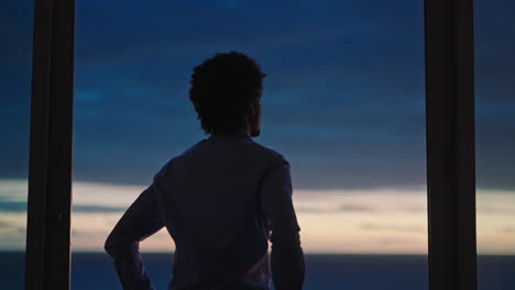 young business man looking out window in hotel room at sunset planning ahead enjoying beautiful ocean view