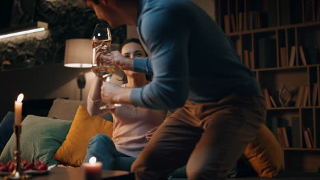 romantic husband bringing wine to smiling wife sitting couch. couple having date