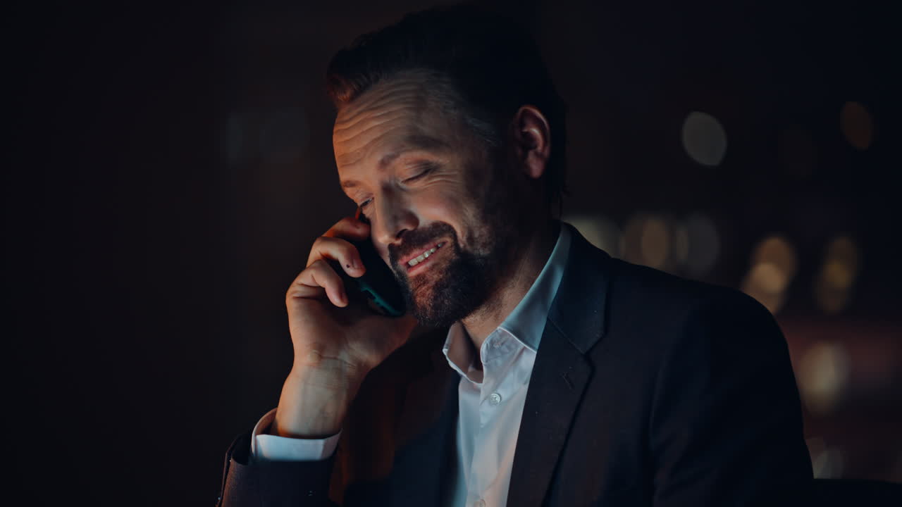 Portrait late worker calling cellphone at dark cabinet. Smiling ceo man talking