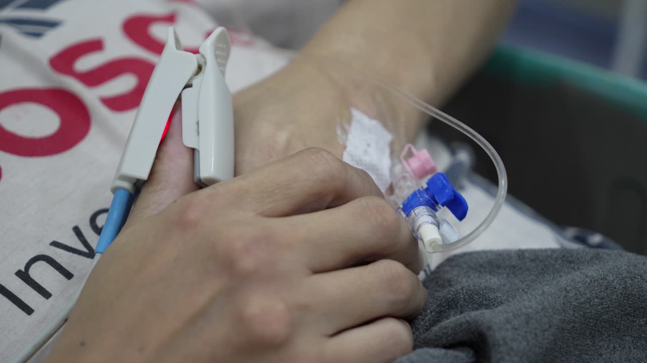 Primo piano della mano di un paziente con flebo e pulsossimetro in ospedale, scena medica.
