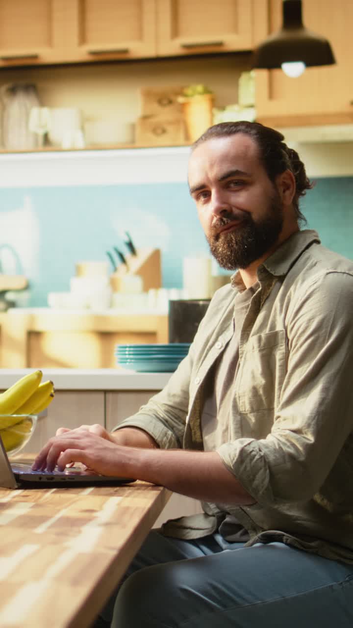 Video verticale: Ritratto di dipendente che usa il laptop al tavolo della cucina per lavoro da remoto