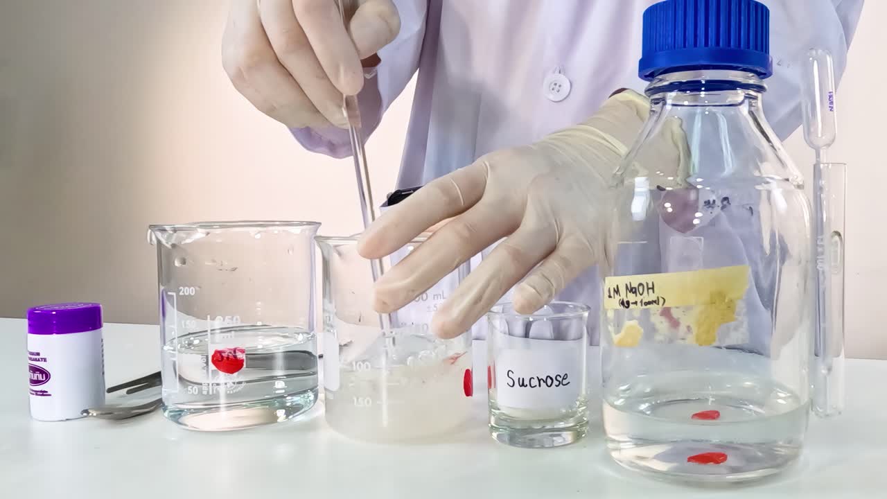 A scientist mixes clear and colored solutions in beakers using a pipette in a lab setting.