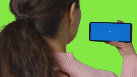 vista trasera de la mujer transmitiendo contenido a la pantalla azul del teléfono móvil contra la pantalla verde