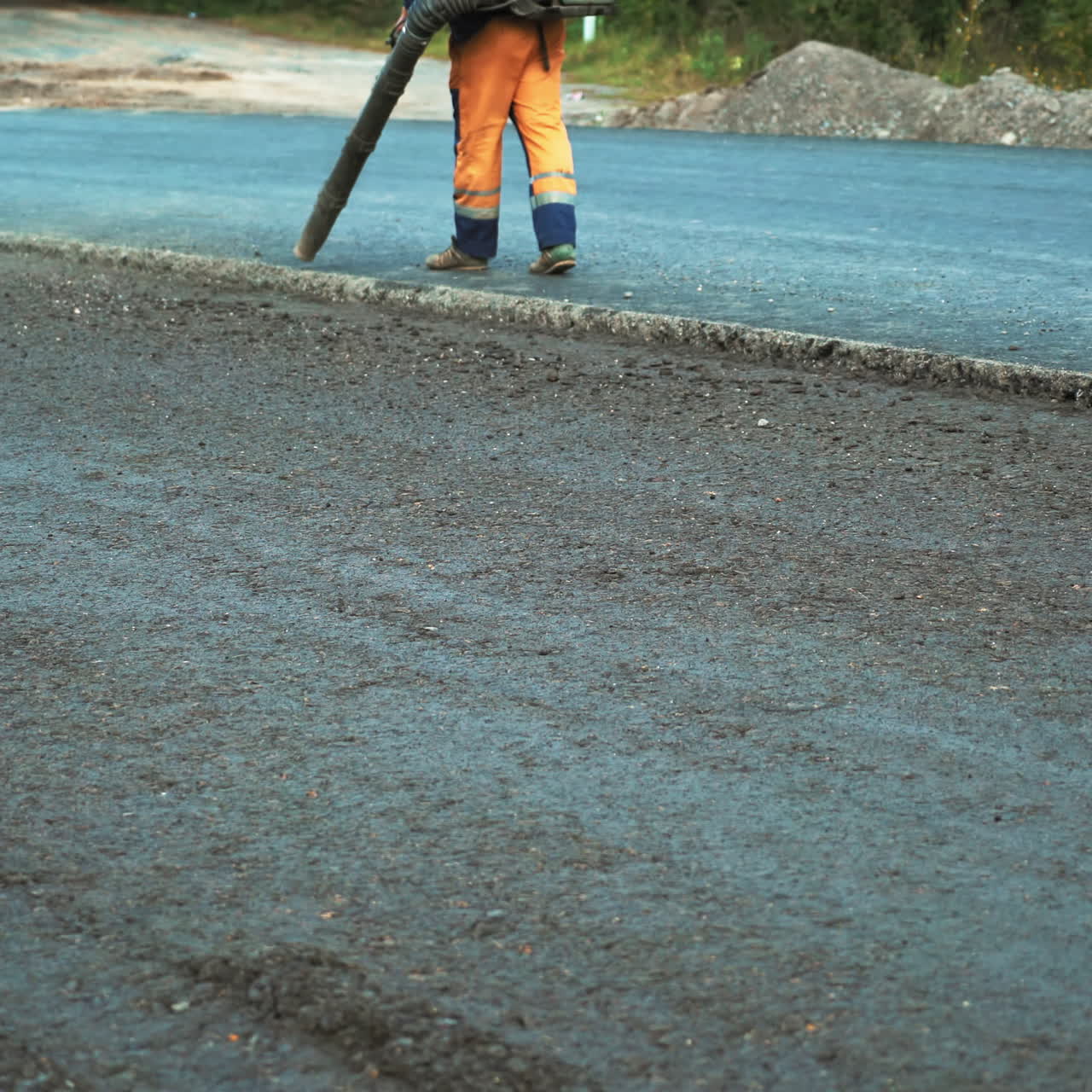 Preparation for a paving on the road. Worker is using compressed air to blow off dust and old asphalt particles from the road.
