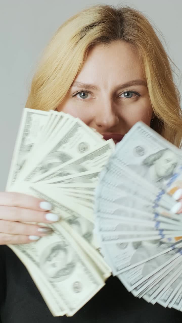 Mulher loira feliz abanando pilhas de notas de cem dólares