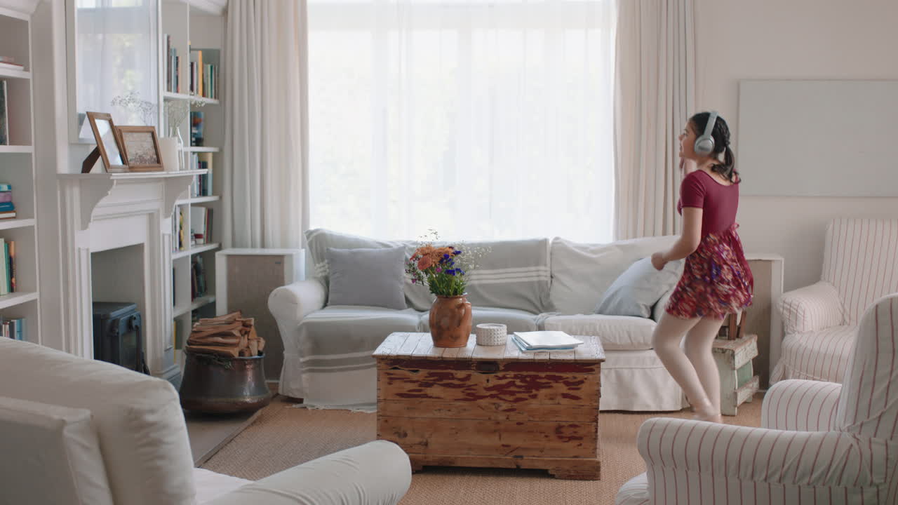 행복한 십대 소녀가 춤을 추고 집에서 발레 춤 동작을 연습하고 음악을 듣고 헤드폰을 착용하고 재미있게 주말을 즐기고 있습니다.